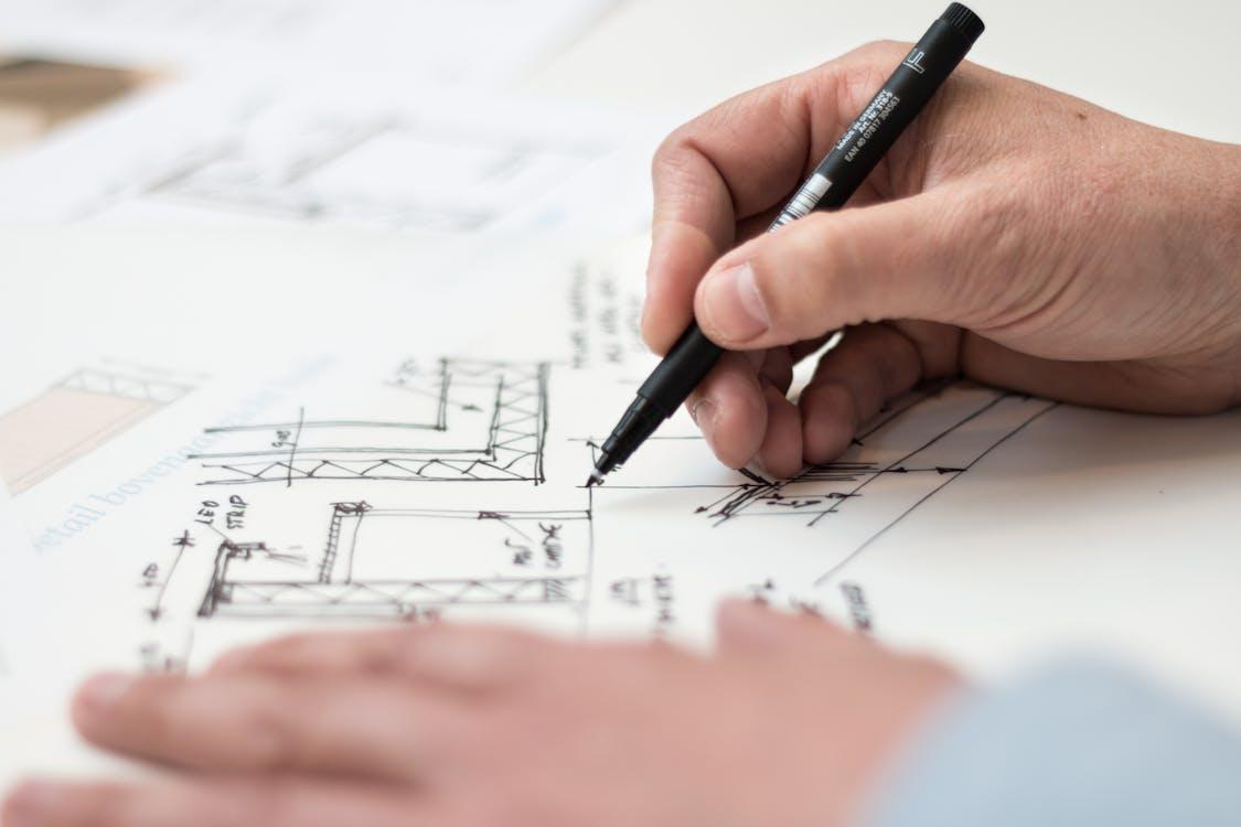 person sketching a modular home design with a pen on paper