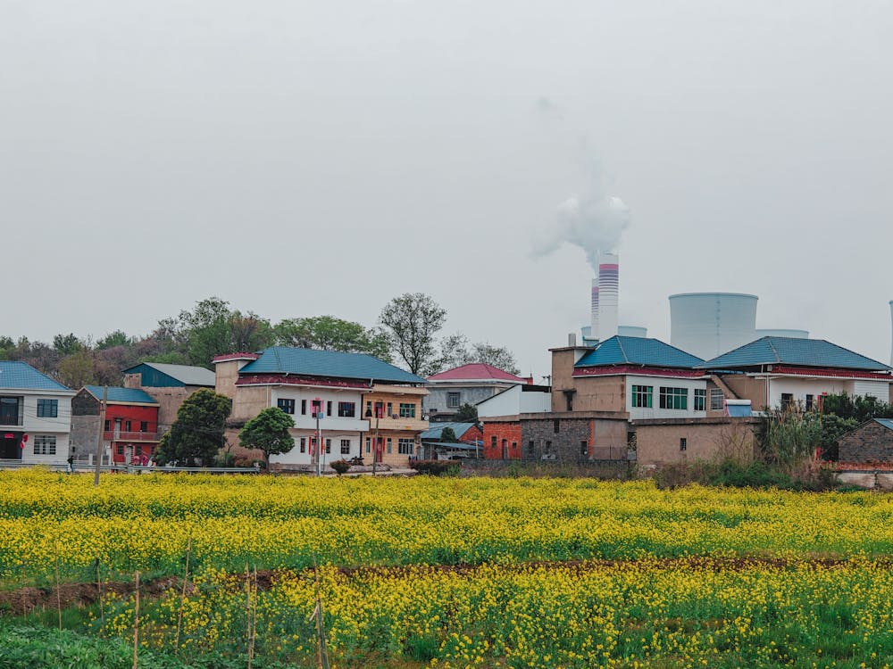 A panoramic view showing a rural village with fields in the foreground and modern industrial buildings in the distance.