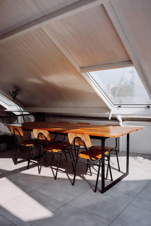 A minimalist attic space with a small round dining table and chairs under angled ceiling beams.