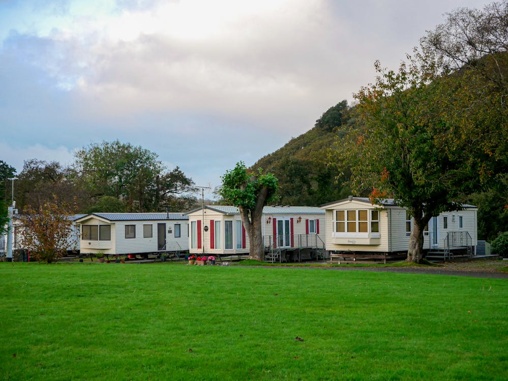 A peaceful row of mobile homes set in a lush countryside with open grassy fields and a mountain backdrop.