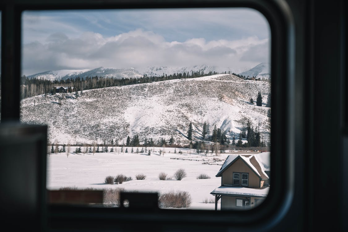 A snowy mountain view framed by a window inside a warm, rustic home interior.