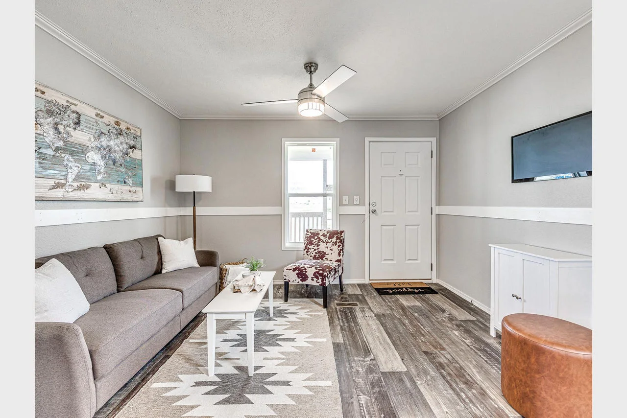 A living room with rustic flooring, gray couch, and mounted TV on the wall